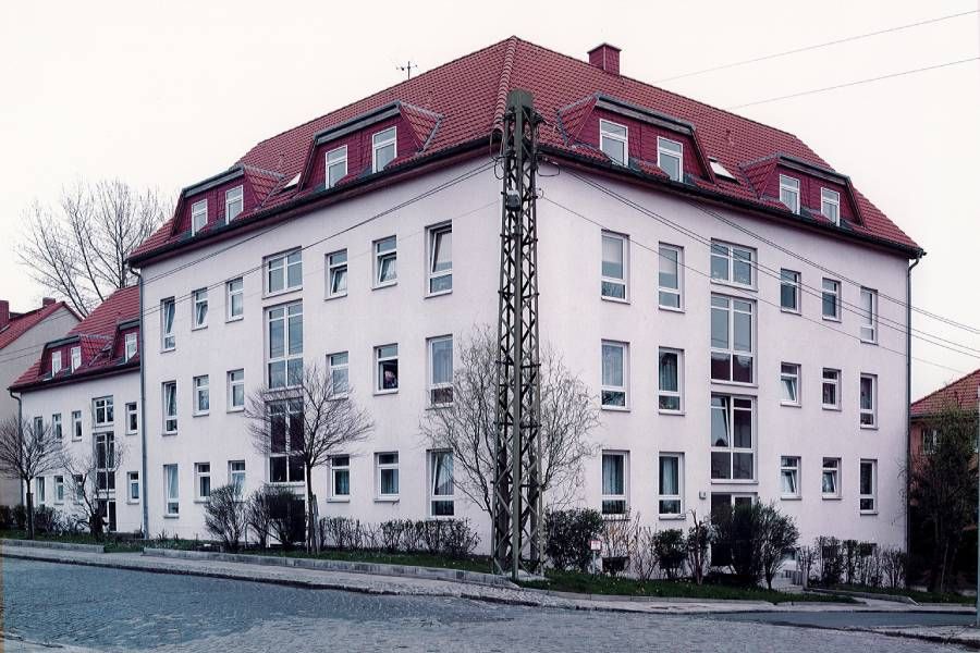 weißes Mehrparteien-Eckhaus mit rotem Dach und vielen Fenstern